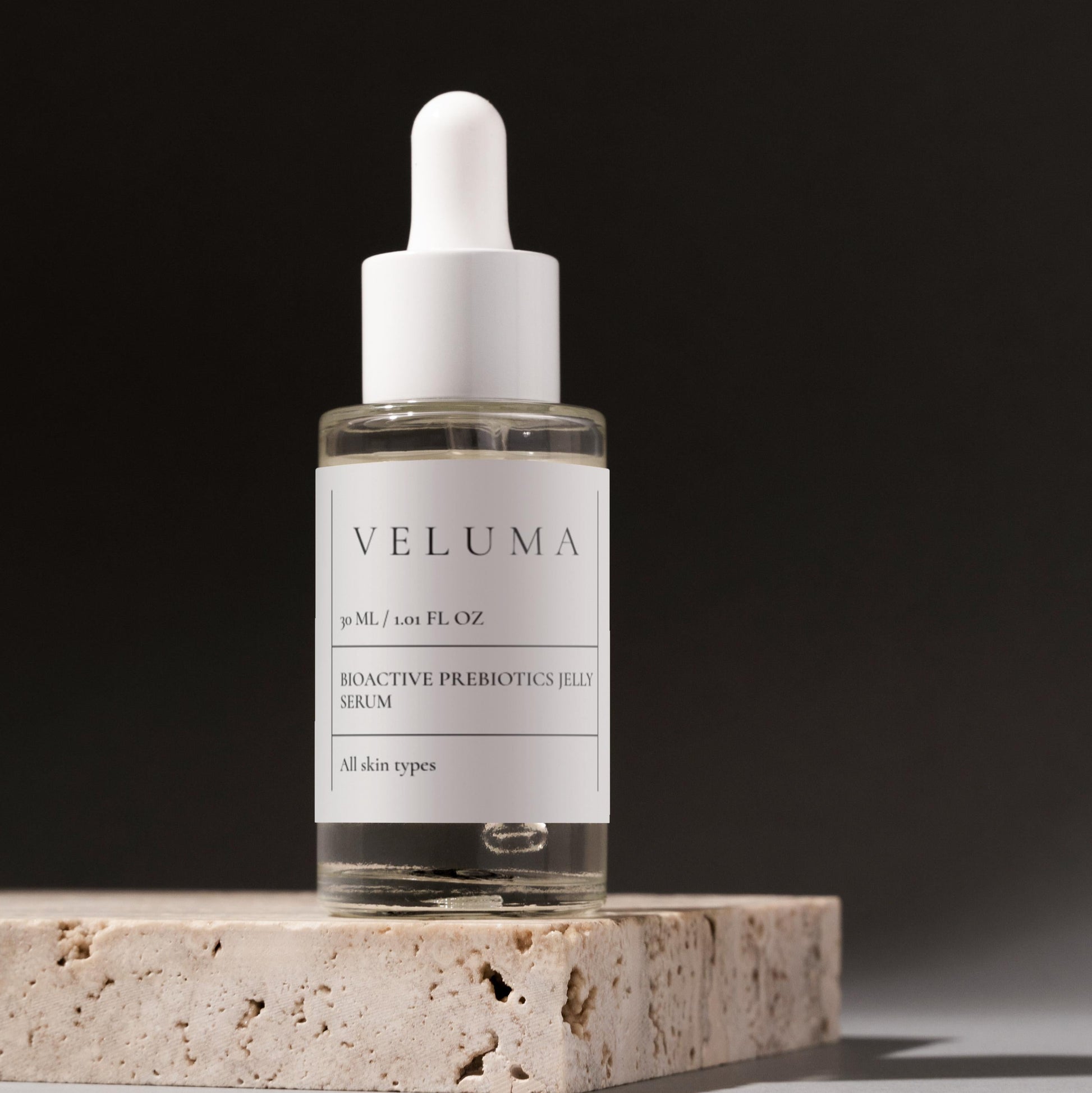 Veluma serum bottle on a stone surface with a dark background